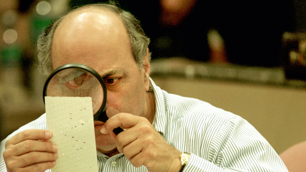 Judge Robert Rosenberg uses a magnifying glass to examine a dimpled chad on a punch card ballot November 24, 2000 during a vote recount in Fort Lauderdale, Florida. (Photo by Robert King/Newsmakers)