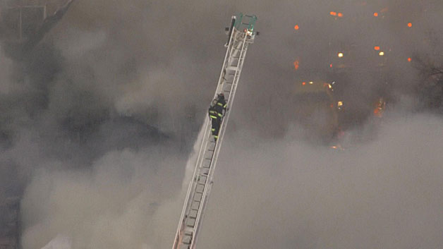 A firefighter ascends a ladder over the 10-alarm blaze. (WBZ-TV)