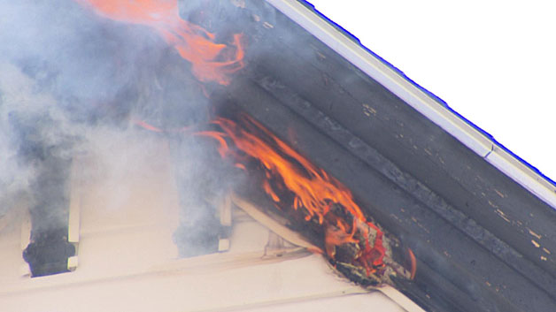 Flames shoot out of the peak of the roof at a East Boston apartment house. (WBZ-TV)